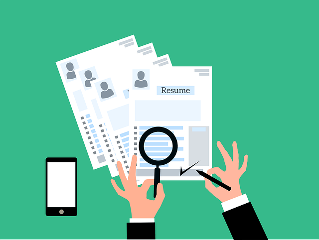 A person using a magnifying glass to read between resumes